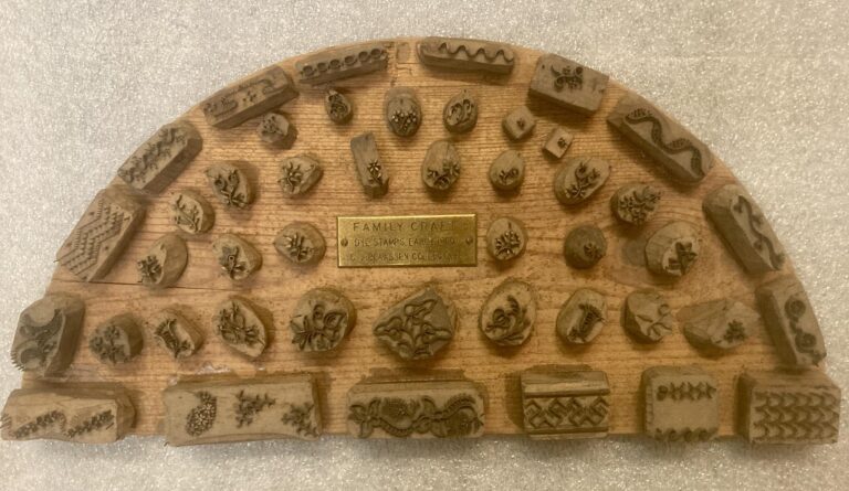 A half-circle wood block with raised stamps used to decorate hand-made aprons, from the late 19th/early 20th century.