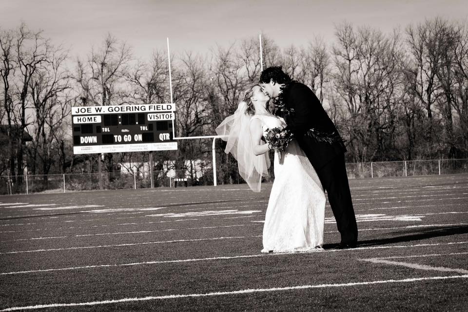 Wedding photo of Sarah Thompson & Peivi Tauiliili on the football field with scoreboard in the background