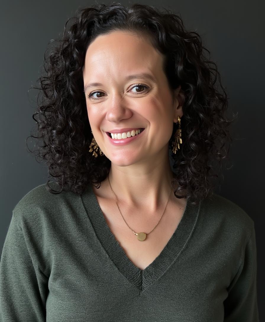 White woman with long, curly dark hair, wearing a dark green V-neck top and a necklace