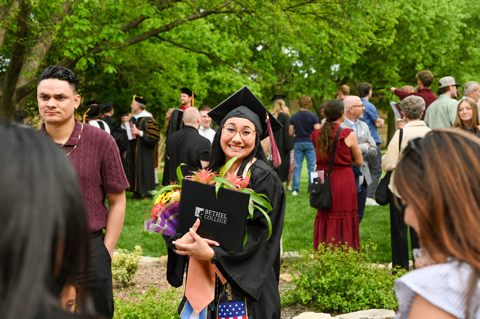 Graduate in cap and gown, holding diploma in its case and an armful of flowers